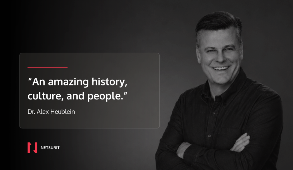 Testimonial quote card over a grayscale portrait: “An amazing history, culture, and people.” by Dr. Alex Heublein, with NETSIRIT logo bottom left.