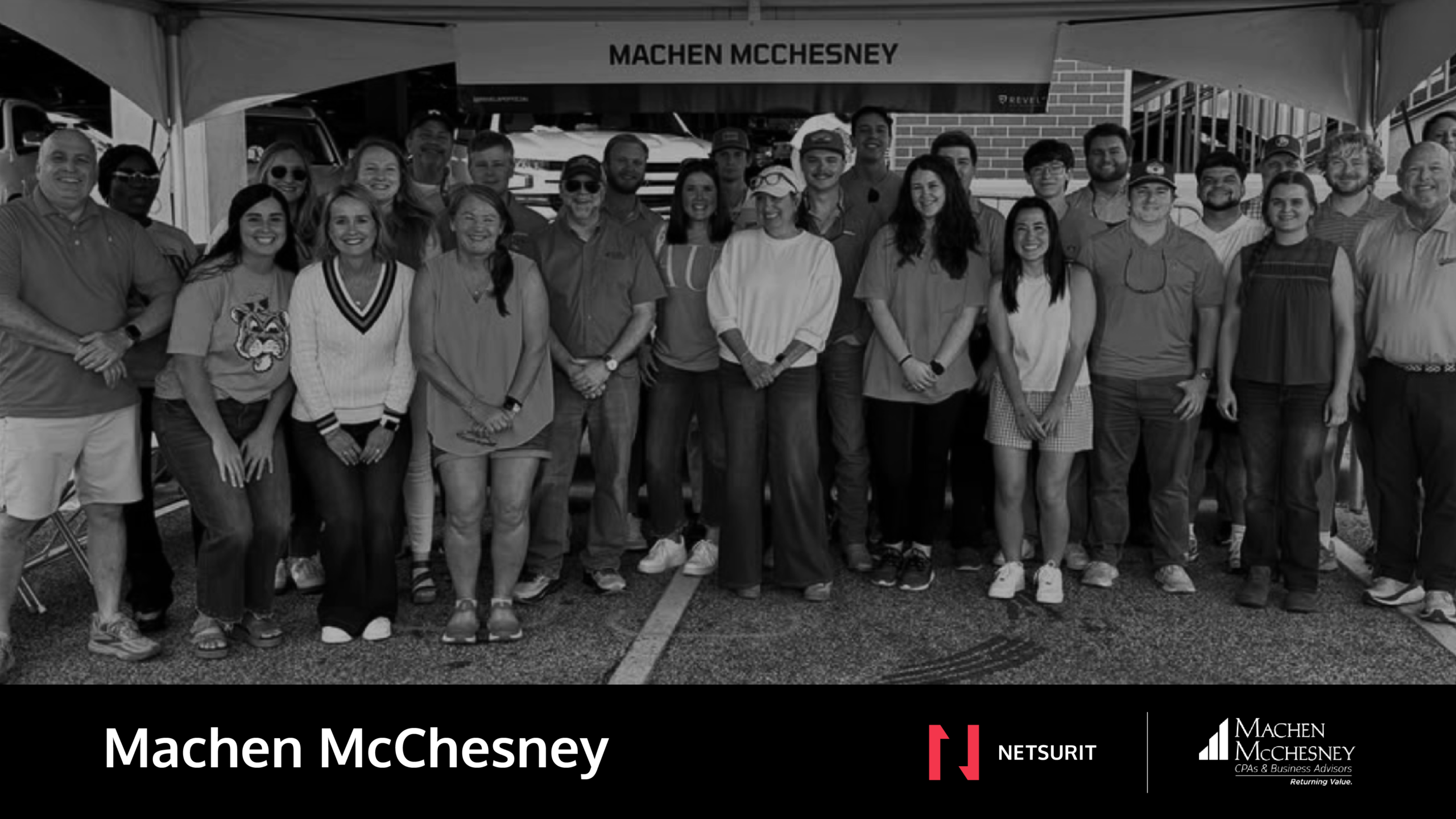 Group of employees posing under a canopy at a Machen McChesney event, smiling at the camera.