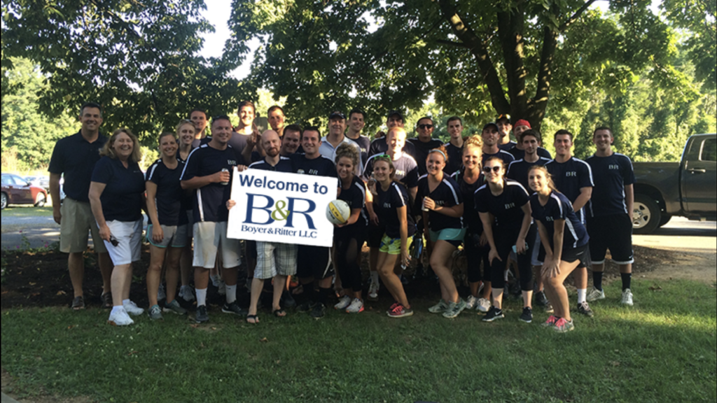 Team photo of coworkers outdoors, holding a banner that reads 'Welcome to B&R Boyer & Ritter LLC'