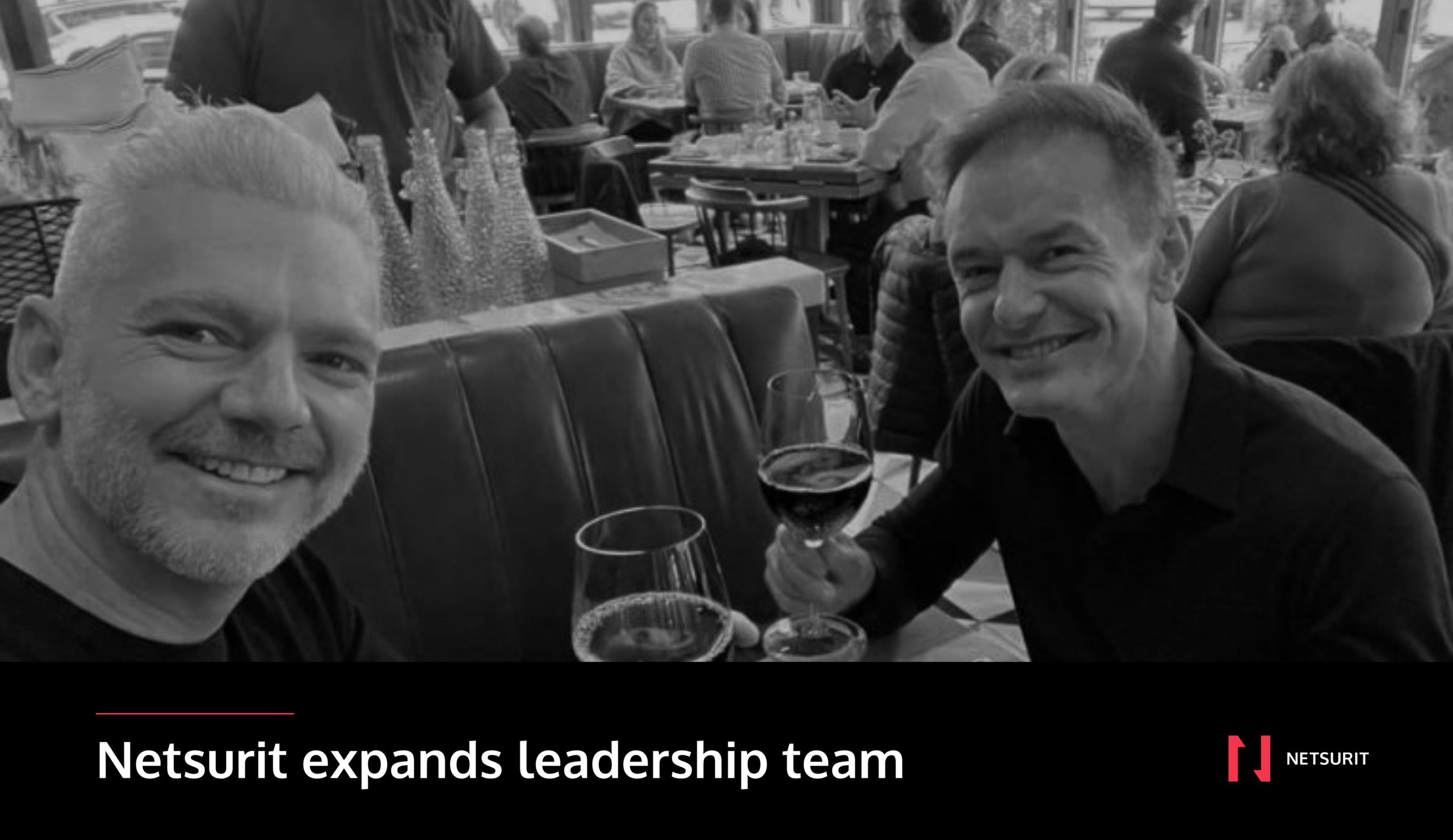 A black and white photo of two men in a restaurant smilling and toasting with a text saying: Netsurit expands leadership team.
