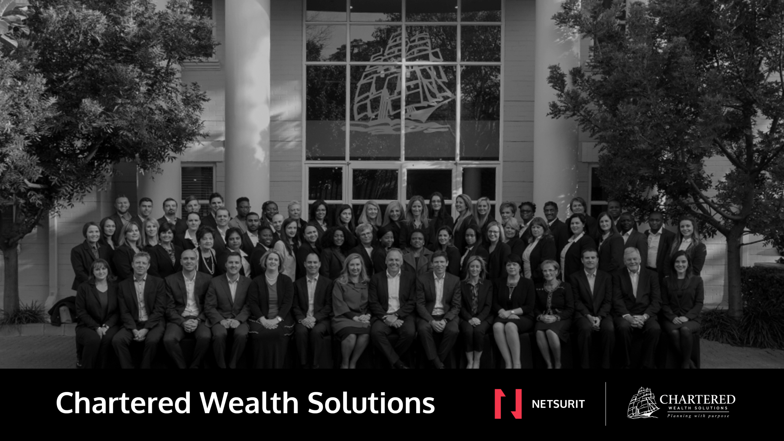 Large group of professionals posed for a team photo outside a modern building; Chartered Wealth Solutions branding at the bottom of the frame.